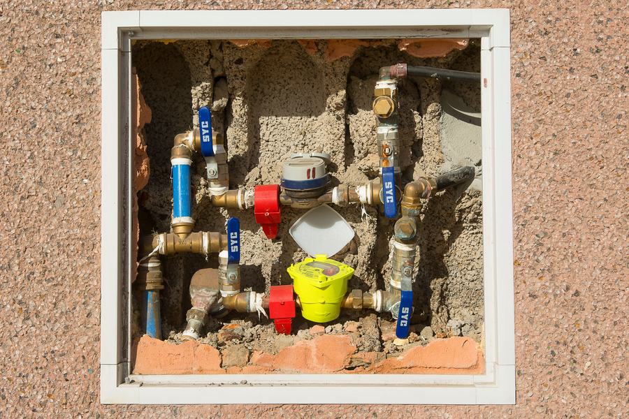 Niche d'un compteur d'eau avec ses vannes à volants bleus et rouges, dans un mur crépi