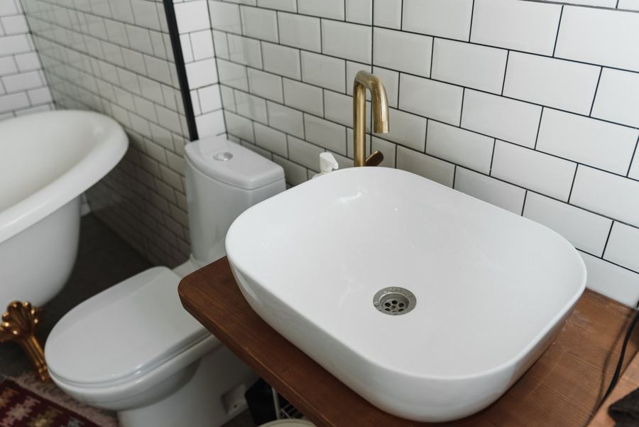 Vasque rectangulaire blanche sur un plan en bois, WC et baignoire sur pieds contre un mur carrelé